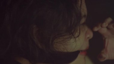 Koyu renk dalgalı saçlı, kısmen aydınlatmalı koyu bir arka planı olan birinin yakın plan profili. Bir kişi derin düşüncelere dalmış gibi görünüyor, bir eli alnına yakın, bir anlık bir yansıma ya da duyguyu işaret ediyor..