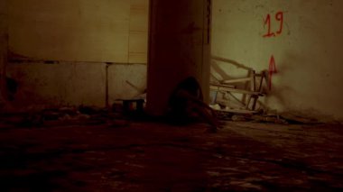 Duvara yaslanmış, loş, terk edilmiş bir yer. Zemin kirli ve molozlarla dolu ve duvarda kırmızı sprey boyayla boyanmış bir numara var. Atmosfer kasvetli ve kasvetli.