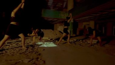 Dansçıların loş ve terk edilmiş bir alanda performans sergilediği dramatik bir sahne. Dansçılar hareket halindeler, etrafa saçılmış enkazlarla güç ve zarafet sergiliyorlar. Atmosfer yoğun ve sanatsal.