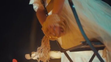 Geceleri sandalyede otururken küçük, tüylü bir köpeği tutan birinin yakın plan fotoğrafı. Arka planda bulanık ışıklar var, rüya gibi bir atmosfer yaratıyor. Kişinin elleri nazikçe köpeği kucaklıyor ve aralarında bir bağ olduğunu vurguluyor..