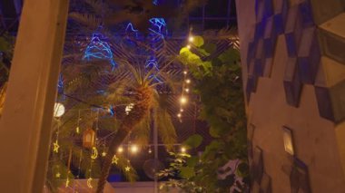 Geceleyin loş bir ara sokak, yıpranmış duvarlar ve manzarayı aydınlatan bir sokak lambası. Atmosfer sessiz ve tüyler ürpertici. Işığın yansıttığı gölgeler var. Uzakta birkaç park edilmiş araç görülüyor, konutlarla çevrili..