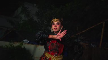 Geleneksel giyinmiş bir kadın gece kültür dansı yapıyor. Süslü takılar takıyor ve bir başlık takıyor, dramatik bir makyajla ifadelerini vurguluyor..