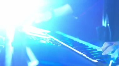 Mavi sahne aydınlatmalı klavye çalan kişinin yakın çekimi.