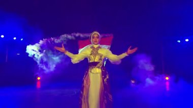 Renkli, dumanlı bir ortamda dramatik ışıklandırmayla bayrak sallayan bir insan..