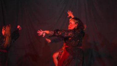 Üç kişi loş bir sahnede renkli kostümlerle geleneksel dans gösterisi yapıyor..