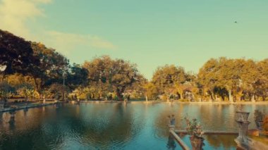 Bereketli yeşillik ve ağaçlarla çevrili sakin bir göletin olduğu sakin bir manzara. Su, mavi gökyüzünü ve etrafındaki yeşillikleri yansıtır. Huzurlu bir atmosfer yaratır..