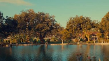 Bereketli yeşillik ve ağaçlarla çevrili sakin bir göl içeren sakin bir manzara. Sahne, su yüzeyindeki yansımalarla ve açık mavi gökyüzüyle doğanın sükunetini yakalıyor..