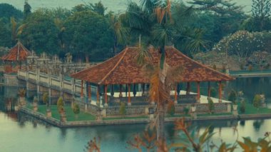 Bereketli yeşillikler ve sakin bir göletle çevrili geleneksel bir Bali pavyonunun huzurlu manzarası. Çadırın sazdan bir çatısı var ve bir ağaç zeminine ve uzak tepelere karşı kurulmuş..