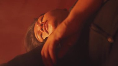 Arka planda bulanık bir yüz olan bir kişinin kumaşı tutarken çekilmiş yakın plan fotoğrafı. Işık sıcak ve karamsar, samimi bir atmosfer yaratıyor..