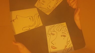 Yansıtıcı bir yüzeye dizilmiş dört soyut portreden oluşan yaratıcı bir görüntü. Çizimlerde, sanatsal eserleri tutan ellerle çevrili, çeşitli ifadelere sahip basit yüz çizgileri sergileniyor..