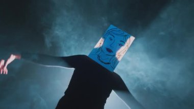 Önünde duran kağıdın üzerine çizilmiş bir yüz çizilmiş bir figür, yumuşak mavi bir ışıkla aydınlatılmış, arkasında duman olan gizemli bir atmosfer yaratıyor..