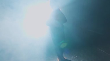 Yüzünü kaplayan bir çizimle dumanlı bir ortamda parlak bir ışıkla aydınlatılan bir insan gerçeküstü bir atmosfer yaratıyor..