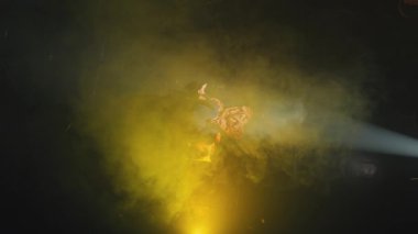 Sahnede, renkli duman ve dramatik ışıklandırmayla çevrili canlı bir atmosfer yaratan bir sanatçı..