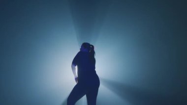 Dramatik ışıklandırma altında dans eden, etkileyici hareketler sergileyen bir dansçı. Arka planda, dinamik atmosferi geliştiren mavi ve kırmızı renklerin bir gradyanı yer almaktadır..