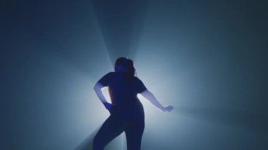 Bir dansçı arkasında çarpıcı bir siluet etkisi yaratan parlak bir ışıkla aydınlanan koyu bir arka plana çarpıcı bir şekilde poz verir..