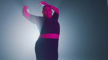 Sahnede dramatik ışıklandırmayla gösteri yapan bir dansçı. Arka planda parlak bir ışık kaynağı var, bir siluet etkisi yaratıyor. Dansçı dinamik bir pozda, hareketini ve enerjisini gösteriyor..