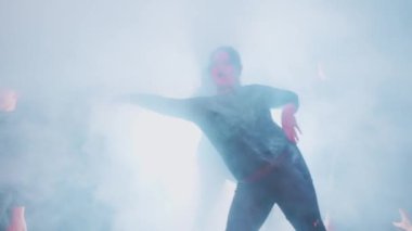 Siluetli dansçılar sahnede dramatik ışık ve duman efektleri göstererek mistik bir atmosfer yaratıyorlar..