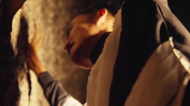 Loş bir çevrede bir dağcı, bir kaya yüzeyine odaklanıyor. Tırmanışçının yüzü kısmen gizlenmiş, tırmanıştaki efor ve konsantrasyonu vurguluyor. Işık dramatik gölgeler yaratır, sahnenin yoğunluğunu arttırır..