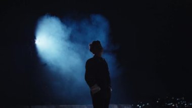 Mavi dumanlı ya da sisli karanlık bir arkaplanda duran bir kişinin silueti. Sahne gizemli ve atmosferik bir atmosfer yaratıyor, figürün ana hatlarını vurguluyor..