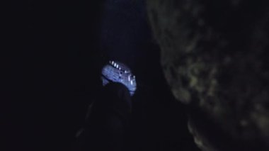 Karanlık, kayalık bir çevrede, soluk bir ışıkla aydınlatılmış bir insanın dar görüşü. Sahne, gölgeler ve dokuların gizemli bir atmosfer yarattığı bir keşif ya da macera hissini akla getiriyor..