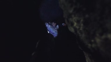 Bir insan dar ve karanlık bir uzayda kapana kısılmış gibi görünüyor, tek eliyle uzanıyor. Sahne loş bir şekilde aydınlatılmış, acil bir durum ve izolasyon hissi yaratıyor..