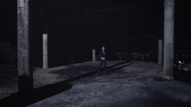 Geceleri ıssız bir çatıda, şehir ışıklarıyla çevrili ıssız bir figür duruyor. Sahne loş bir ışıkla aydınlatılmış ve gölgeli gizemli bir atmosfer yaratılmış..