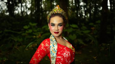 Ronggeng adında geleneksel bir dansçı sabah vakti büyük bir zarafet ve çarpıcı kırmızı kostümle ormanda duruyor.