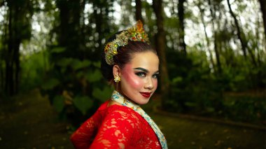 Bir Cava dansçısı şık bir kırmızı kostüm giyer ve sabahları ormanda dans ederken sergilediği zarafetin altını çizer.