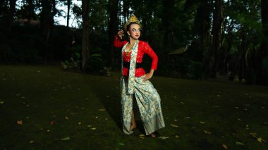 Geleneksel Endonezyalı bir dansçı, güzel görünüşüyle sabah ormanda seyircilerin dikkatini çeken kırmızı bir kostüm giyerken göz kamaştırıyor.