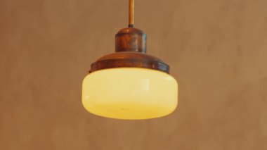 Yuvarlak, buzlu cam gölgeli ve pirinçten armatürleri olan klasik tarzda bir kolye. Sıcak, desenli bir arka planda asılı..