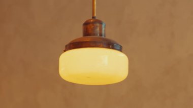 Yuvarlak, buzlu cam gölgeli ve pirinçten yapılma bir lamba, tavandan sarkan desenli bej bir arka plan..