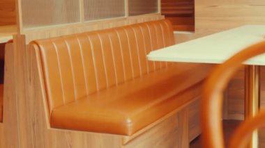 Kahverengi deri koltuklu, dikey dikişli, ahşap bir masa ve sıcak ahşap panelle tamamlanmış samimi bir restoran..