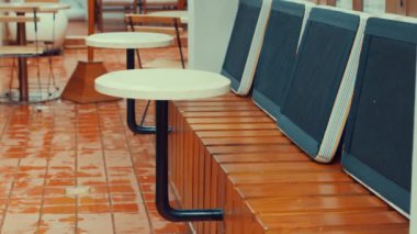 Ahşap bankları ve fayanslı döşeme üzerinde yuvarlak masaları olan açık hava oturma alanı.