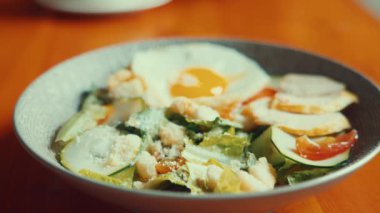 Bir kase taze yeşillik, dilimlenmiş salatalık, domates ve ızgara tavuk, üstüne de peynirli yumurta serpiştirilmiş..