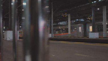 Bulanık treni olan bir tren istasyonu platformu. Sahnede metal sütunlar ve tren bilgilerini gösteren tabelalar yer alıyor. Atmosfer kentsel ve dinamik, toplu taşımanın özünü yakalıyor..