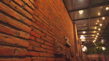 Yukardan gelen yumuşak ışıklandırmayla aydınlatılan, sıcak tonlu, kırsal tuğla bir duvarın yakın çekim görüntüsü. Mekan, muhtemelen bir kafe ya da restoranda rahat bir atmosfer olduğunu gösteriyor..