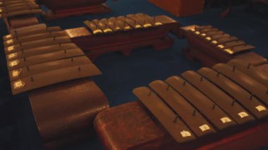 Geleneksel müzik aletlerinin dairesel bir şekilde dizilmiş yakın plan görüntüsü. Enstrümanların ahşap çerçeveleri ve metal parmaklıkları var. Karmaşık işçilik sergiliyorlar. Arkaplan, araçların görsel çekiciliğini artıran koyu mavi bir renktir..