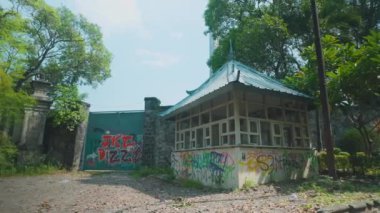 Geleneksel çatısı olan terk edilmiş bir yapı. Etrafı fazla gelişmiş bitki örtüsü ve duvarlarda graffitilerle çevrili. Sahne ıssız bir yerde, arka planda büyük bir kapı var..