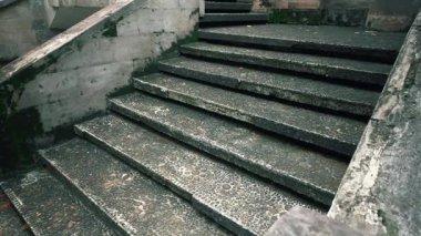 Yosun ve basamaklara gömülü küçük taşların yer aldığı dokulu bir yüzeyi olan yıpranmış taş merdivenlerin yakın görüntüsü. Merdivenler kısmen gölgeli, karamsar bir atmosfer yaratıyor..