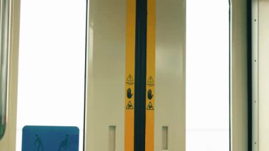 Uyarı işaretleri ve ulaşılabilir oturma yerlerini gösteren mavi bir sembolle metro kapısının iç görüntüsü..