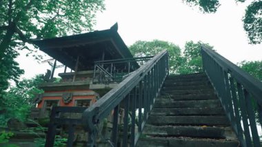 Yeşilliklerle çevrili geleneksel bir tapınağa çıkan taş bir merdiven. Tapınak karmaşık mimari detaylara sahip ve ağaçlar tarafından kısmen gizlenmiş..