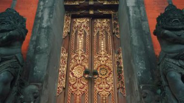 Altın aksanlı süslü ahşap kapılar ve iki taş koruyucu heykelle çevrili güzel bir Bali tapınağı girişi..