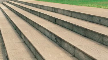 Düz bir yüzeye sahip beton merdiven seti yukarı doğru çıkıyor. Merdivenler doğrusal olarak dizilmiş, arka planda çimenlik bir alan var..
