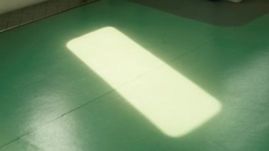 Yeşil zeminde yumuşak, dikdörtgen bir ışık demeti, sakin ve minimalist bir atmosfer yaratıyor..