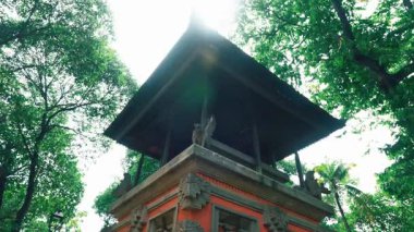 Geleneksel bir Bali tapınağı yapısı. Etrafı yemyeşil ağaçlarla çevrili. Güneş ışığı yukarıdan parlıyor ve huzurlu bir atmosfer yaratıyor..