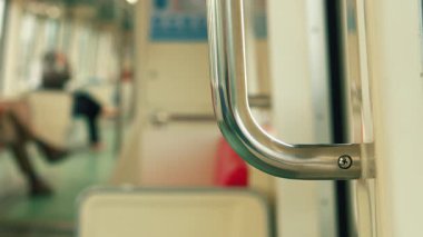 Metalik bir trenin tırabzanına yakın plan, arka planda bulanık yolcular. Odak noktası, tırabzanın parlak dokusu ve şehir seyahati hissi..