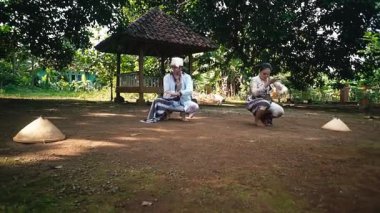 İki dansçı, geleneksel danslarını açık havada yapıyorlar. Kültürel kıyafetlerini ve dışavurumcu hareketlerini sergiliyorlar..