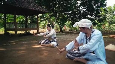 Doğal bir ortamda geleneksel dans eden iki kadın. Geleneksel kıyafetler giyiyorlar, zarif el hareketleri sergiliyorlar ve yerde oturuyorlar..