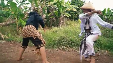 Geleneksel giysiler giymiş iki kişi kırsal bir alanda eğlenceli bir dans ya da performans sergilerler..