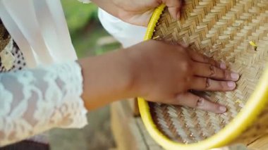 Dokuma sepetinde suyla yıkanan ellerin yakın çekimi. Sahne bir bağ ve gelenek anı yakalıyor, sepetin dokusunu ve suyun nazik akışını vurguluyor..